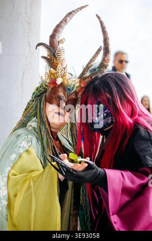 Venezia, Italia - 8 febbraio 2026: Due donne che indossano maschere e costumi ornati con corna si mettono insieme al Carnevale di Venezia, mettendo in risalto il loro distaccamento Foto Stock