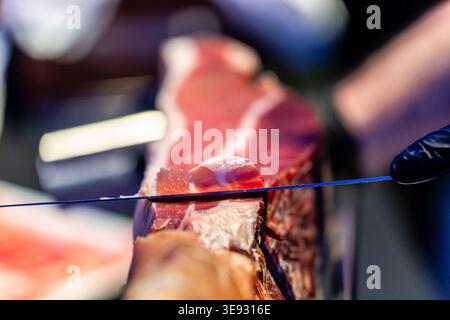 Affettare a mano porzioni sottili e delicate di prosciutto con un coltello affilato da intagliare per assaggiare presso una gastronomia Foto Stock