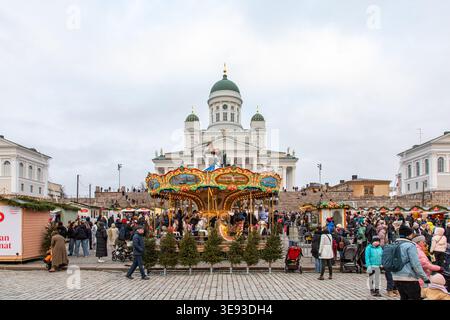 Persone al Tuomaan Markkinat o al mercato di Natale di Helsinki in Piazza del Senato con la giostra veneziana di fronte e la cattedrale di Helsinki sullo sfondo Foto Stock