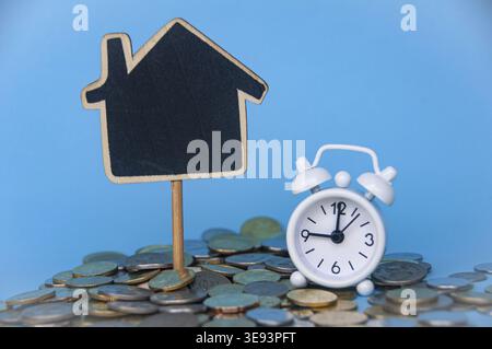 Monete d'oro sparse, sveglia e casa modello vuota con spazio personalizzabile per testo o idee . Copiare spazio e concetto di investimento Foto Stock