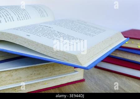 Un libro aperto con copertina rigida che poggia su una pila di libri con pagine leggermente sollevate come se fosse letto in un ambiente di studio tranquillo Foto Stock