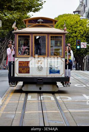 Una funivia si sposta lungo i binari di San Francisco. La gente si diverte mentre attraversa la città in una giornata di sole. Foto Stock