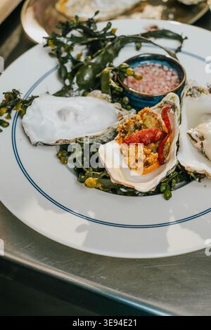 Un piatto di cibo con un bordo blu e bianco. Il piatto contiene una varietà di cibi, tra cui ostriche, verdure e una salsa. La piastra è posizionata su un Foto Stock