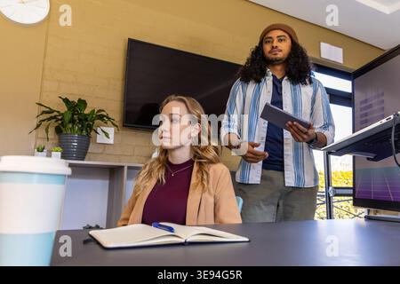 Colleghi diversi che discutono idee al tavolo dell'ufficio, donna che scrive su un notebook, uomo che tiene un tablet Foto Stock