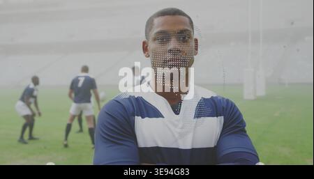 Giocatore di rugby maschile in piedi che indossa una maglia blu e bianca con cappuccio sul campo di erba, palla da rugby visibile Foto Stock