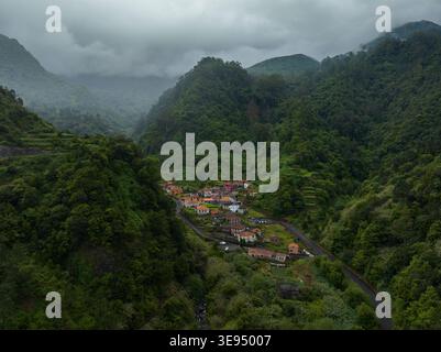 Vista aerea del villaggio di Caminho da Ribeira grande, immerso in una lussureggiante valle verde con ripide colline boscose e basse nuvole a Funchal, Madeira, porto Foto Stock