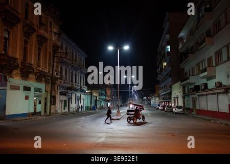 Una persona cammina lungo una strada vuota di notte mentre un triciclo motorizzato aspetta di fianco. Foto Stock