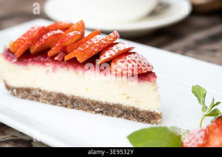 Un pezzo di deliziosa cheesecake con frutti di bosco su un vero tavolo da caffè da vicino. Tazza di caffè sullo sfondo Foto Stock