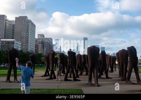 Una persona si trova di fronte a un grande gruppo di sculture in bronzo, alzando la mano come se si scattasse una foto. Le sculture sono disposte in file attraverso a. Foto Stock