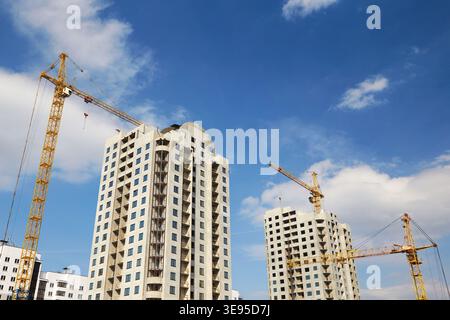 Vista dal basso degli alti edifici costruiti con gru da costruzione Foto Stock