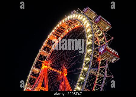 Ruota panoramica illuminata di notte con cabine passeggeri che ruotano in un parco divertimenti all'aperto contro un cielo buio. Foto Stock