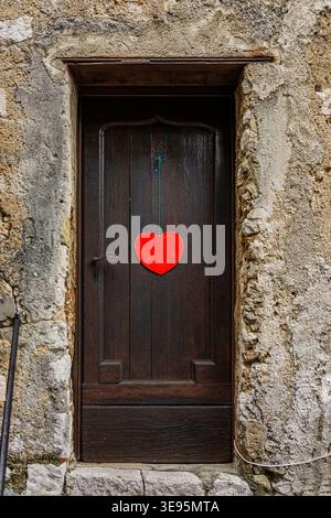 una porta frontale di legno scuro con un cuore rosso al centro Foto Stock