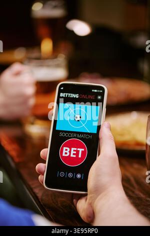 Scommessa su smartphone per adulti in mano su una partita di calcio al pub Foto Stock