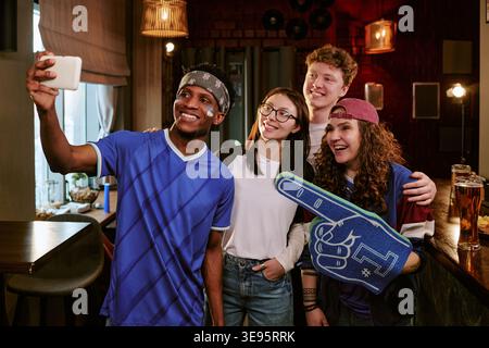 Amici multietnici che prendono Selfie mentre sostengono la squadra nel bar dello sport Foto Stock