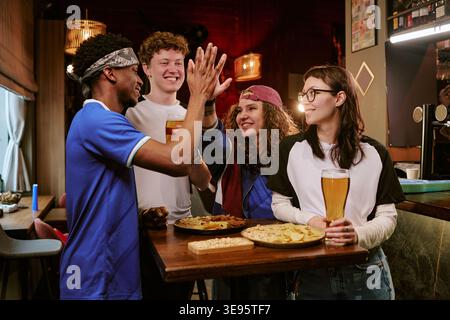 Amici diversi che celebrano lo sport, Win in Bar con bevande Foto Stock