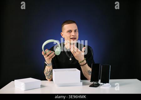 Ritratto di un giovane uomo caucasico adulto che presenta cuffie wireless durante lo streaming di unboxing. Utile per il marketing degli influencer, la revisione dei prodotti, la promozione e-commerce, il medium shot Foto Stock