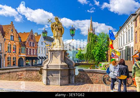 Bruges, Belgio, 5 luglio 2023: Monumento alla statua di Sanctus Joannes Nepomucenus sul ponte, argine del canale di Dijver, edifici medievali nel centro storico di Bruges, Foto Stock