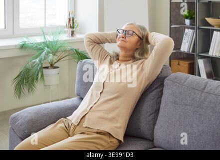 Donna matura e tranquilla in abiti informali seduti su un comodo divano che riposa a casa Foto Stock