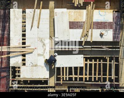 Vista aerea della costruzione di edifici e casseforme con un lavoratore che installa pannelli di legno in un sito a New Taipei, Taiwan. Foto Stock