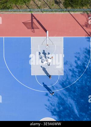 Veduta aerea di persone che giocano a basket su un vivace campo all'aperto blu e rosso con lunghe ombre e un cerchio a Taiwan. Foto Stock