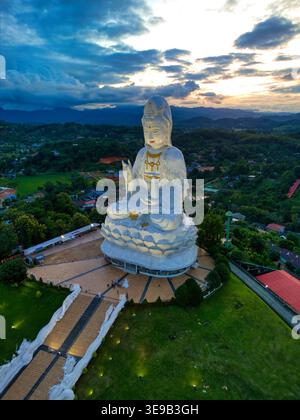 Vista aerea dell'imponente statua bianca di Guan Yin al complesso del tempio Wat Huay Pla Kang sotto un suggestivo cielo al tramonto con colline verdi a Tambon Ba Foto Stock