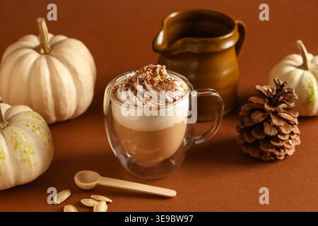 Bicchiere di latte di zucca caldo con panna montata e semi su sfondo marrone Foto Stock