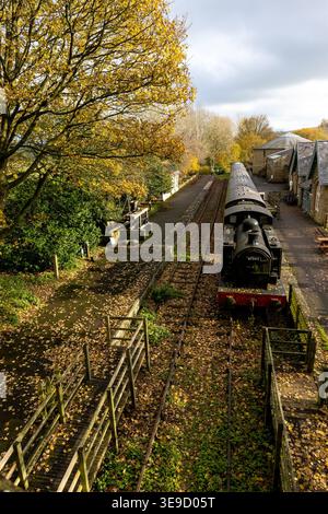 Locomotiva a vapore d'epoca alla stazione di Hawes a Wensleydale, circondata da alberi autunnali e foglie cadute sulla piattaforma Foto Stock
