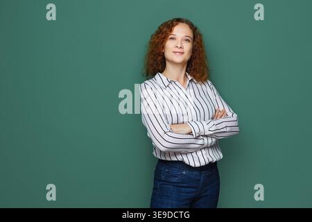 Donna d'affari sorridente che posa con le braccia piegate e guarda la fotocamera su uno sfondo colorato Foto Stock