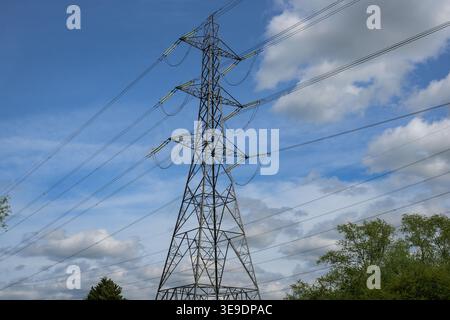 Il pilone di trasmissione dell'energia elettrica si staglia contro un cielo azzurro, mettendo in risalto le infrastrutture di alimentazione, la distribuzione dell'energia e il panorama industriale. Foto Stock