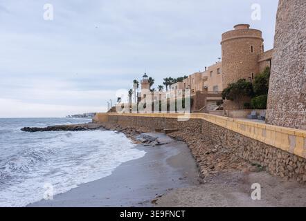 Passeggiata storica con antiche torri e faro sulla costa marina sotto il cielo nuvoloso in Spagna Foto Stock