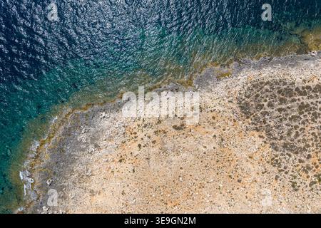 Vista aerea dall'alto verso il basso della costa rocciosa che incontra le limpide acque turchesi del Mediterraneo con le scogliere poco profonde vicino alla baia di St Pauls, Malta. Foto Stock