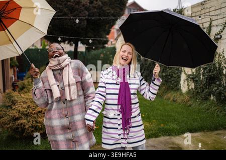 Diverse donne amiche che ridono e tengono gli ombrelli sotto la pioggia Foto Stock