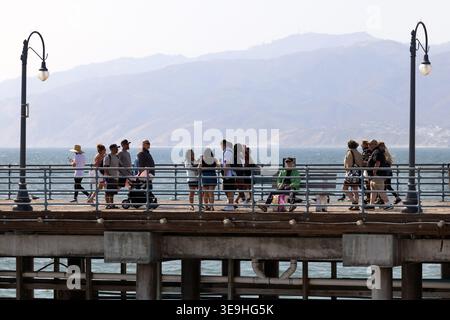 I visitatori camminano lungo il molo di Santa Monica con l'oceano Pacifico e le montagne di Santa Monica sullo sfondo, California, Stati Uniti Foto Stock