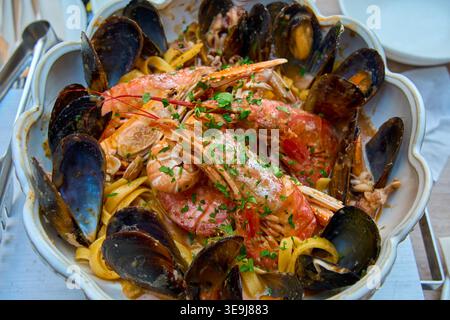 Deliziosa pasta a base di pesce con grandi gamberetti e cozze in una ciotola di ceramica. Linguine mediterranee tradizionali con crostacei ed erbe fresche. Foto Stock