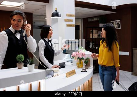 Il turista è assistito da un cordiale receptionist asiatico al banco della reception che spiega le procedure di check in. Il cliente è seduto nell'atrio del confortevole resort e parla con il portiere della prenotazione della camera Foto Stock