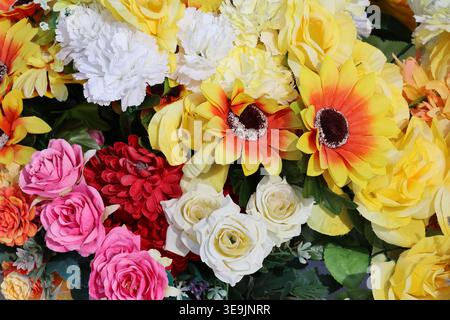 Vivace bouquet di fiori artificiali con rose rosa, crisantemi rossi, margherite bianche e gialle e gerberas arancioni in una disposizione densa Foto Stock