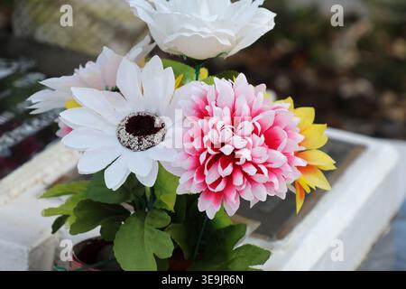 Composizione floreale artificiale con un crisantemo rosa e una margherita bianca collocata su una tomba in pietra o un monumento commemorativo Foto Stock