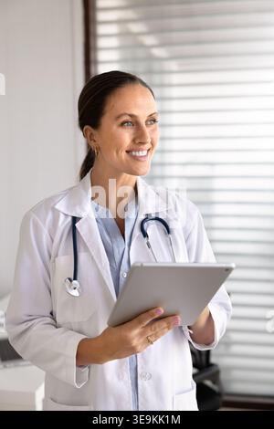 Medico sorridente in piedi in ambulatorio con tablet digitale Foto Stock