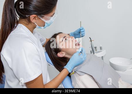 Una dentista sta sta curando un paziente in uno studio dentistico. Il paziente siede su una sedia dentale mentre il dentista utilizza strumenti dentali. Foto Stock
