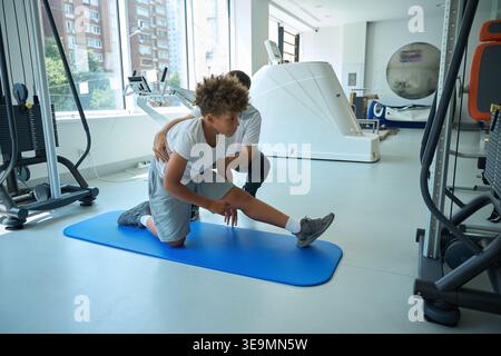 Ragazzo afroamericano che si allunga con un uomo adulto in palestra Foto Stock