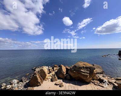 Splendido paesaggio costiero caratterizzato da grandi massi su una spiaggia sabbiosa contro un mare blu profondo e un vivace cielo soleggiato. Foto Stock