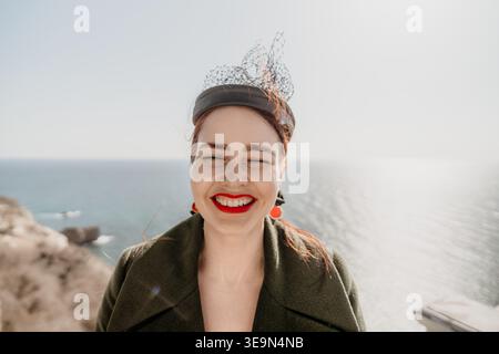 Donna che sorride sulla costa giovane donna gioiosa che indossa un fascinatore ride in riva al mare in una luminosa giornata di sole Foto Stock