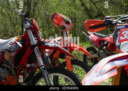 Vladikavkaz, Russia - 18 aprile 2026 : gruppo di moderne motociclette enduro parcheggiate in una foresta durante una giornata di sole con un motocross professionista hel Foto Stock