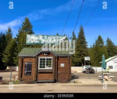Easton, Washington, Stati Uniti d'America - 18 aprile 2026: Piccolo chiosco di caffè drive-thru in una rustica cabina in legno accanto all'autostrada con sfondo sempreverde nella foresta di Easton. Foto Stock