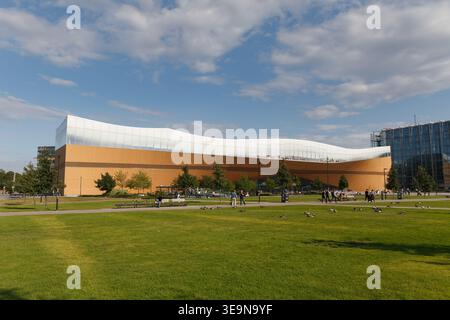 HELSINKI, FINLANDIA - 11 AGOSTO 2025: Moderno edificio culturale con tetto dorato ricurvo adagiato su un prato verde sotto un cielo estivo blu. Foto Stock