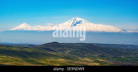 Le montagne innevate dell'Ararat si innalzano sopra le colline ondulate sotto il cielo azzurro. Il paesaggio presenta campi verdi e picchi lontani. Nessun documento d'identità per animali o piante Foto Stock