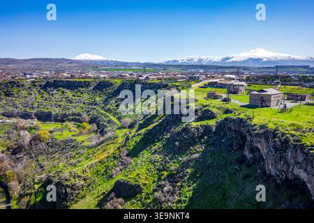 Villaggio immerso nella verde valle con montagne innevate in lontananza. Le scogliere rocciose circondano un lussureggiante terreno erboso. Piccole case punteggiano il paesaggio Foto Stock