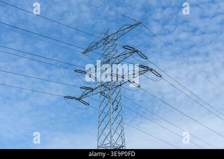 La torre di trasmissione ad alta tensione trasporta linee di alimentazione contro un cielo blu nuvoloso in un ambiente esterno Foto Stock