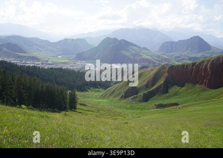 Splendida vista panoramica del monte Zhuo'er con praterie verdi, foreste e scogliere di roccia rossa a Qilian, Qinghai, Cina Foto Stock