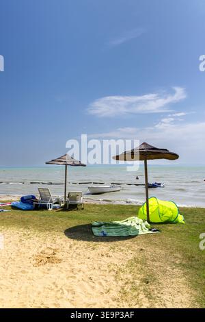 Rilassante spiaggia lungo il lago Balaton, Ungheria, con ombrelloni di paglia e articoli per il tempo libero Foto Stock